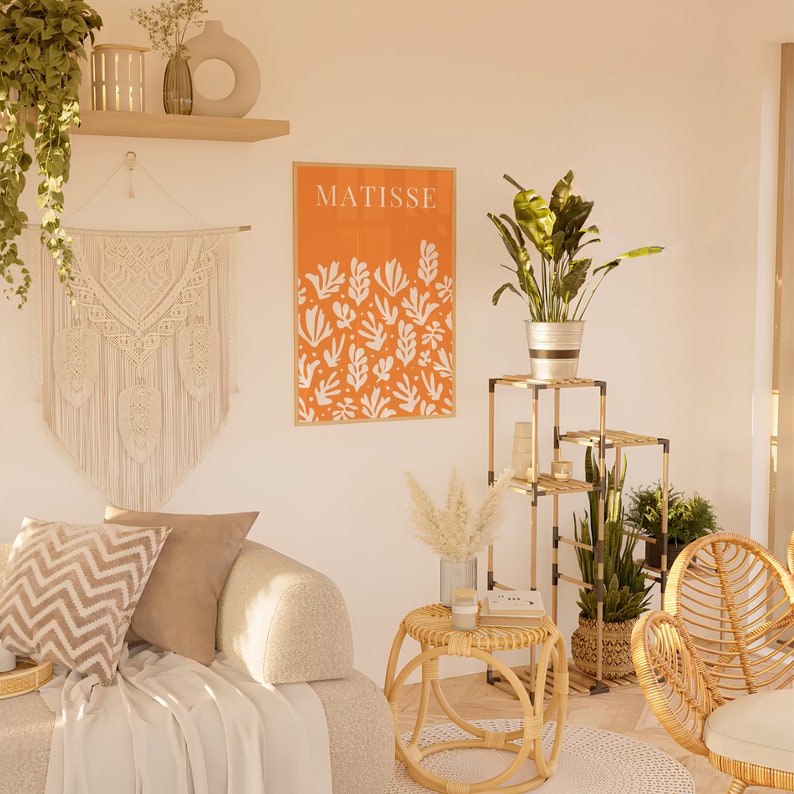 Puede incluir: Un interior de sala de estar con un sof&aacute; blanco, una mesa auxiliar de mimbre, una planta en maceta y una impresi&oacute;n enmarcada con el texto "MATISSE" y un fondo naranja con formas abstractas blancas.