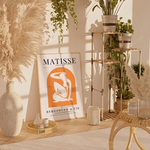 Puede incluir: Una impresi&oacute;n enmarcada de una pintura de Matisse titulada "Painting Decorative" con el texto "BERGGRUEN & CIE" y la fecha "10 Rue de l'Universit&eacute; Paris VIIe.  Du 27 Janvier au 10 Mars 1913". La impresi&oacute;n est&aacute; en una pared blanca con una estanter&iacute;a de madera detr&aacute;s. La estanter&iacute;a tiene plantas y macetas encima.