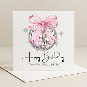 May include: A white birthday card featuring a pink bow and a disco ball illustration. The card reads "Happy Birthday to a Wonderful Sister." The name "Lola" is on the bow. Four starbursts are in the background.