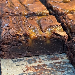May include: Close-up of freshly baked brownies with a rich, dark chocolate colour. The brownies are topped with a layer of caramel, creating a delicious contrast in texture and flavour. The image showcases the moist, fudgy interior.