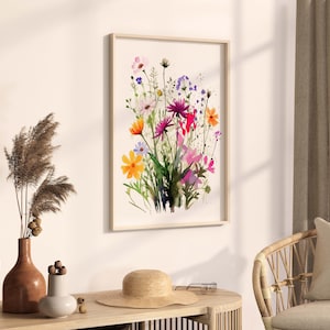 Op de afbeelding: Een ingelijst aquarel schilderij van een boeket kleurrijke wilde bloemen, waaronder roze, paarse, gele en oranje bloemen. De bloemen zijn in een losse, natuurlijke stijl gerangschikt, en de achtergrond is een zacht wit.