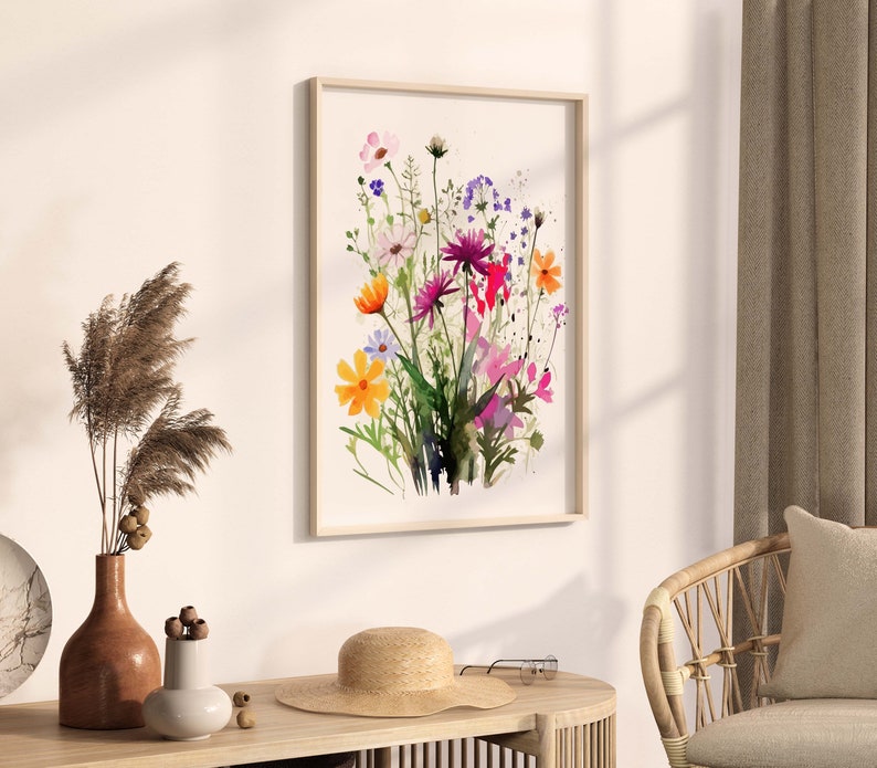 Op de afbeelding: Een ingelijst aquarel schilderij van een boeket kleurrijke wilde bloemen, waaronder roze, paarse, gele en oranje bloemen. De bloemen zijn in een losse, natuurlijke stijl gerangschikt, en de achtergrond is een zacht wit.