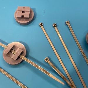 May include: Five gray plastic cable ties and two gray plastic bases with a slot for the cable ties. One base has a gold-colored disc on top.