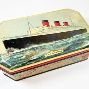 May include: A rectangular metal tin with beveled corners featuring a painted illustration of the R.M.S. Queen Mary ship on the lid. The sides of the tin display the text Bensons English Choice Confections with small decorative graphic elements.