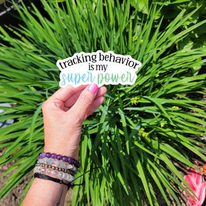 May include: A sticker with the text "tracking behavior is my super power" in black text on a white background with a blue and green gradient.