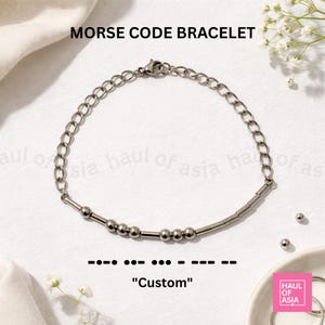 May include: A silver-toned Morse code bracelet with the word "Custom" spelled out in beads. The bracelet features a chain link design and is displayed on a white surface. The text "MORSE CODE BRACELET" is at the top.