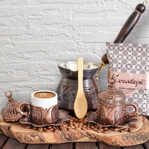 May include: A traditional Turkish coffee set with a copper pot, cups, and a wooden spoon. The set is arranged on a wooden serving tray with coffee beans scattered around. The coffee is packaged in a bag with the brand name "Kocatepe" and the text "Türk Kahvesi" printed on it.