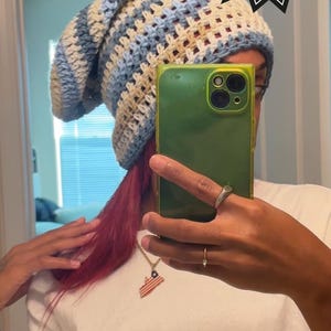 May include: A crochet hat with a blue and beige striped pattern. The hat is being worn by a person with red hair. The image also includes a text overlay that says "Crochet PDF pattern".