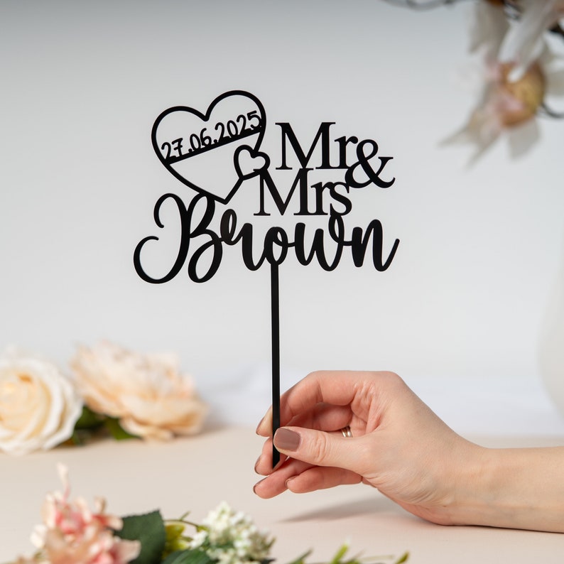 May include: Black acrylic cake topper with the text "Mr & Mrs Brown" and a heart with the date "27.06.2025" inside.