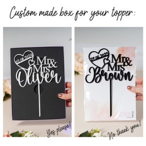 May include: A black and white wedding cake topper with a heart and the text "Mr & Mrs Oliver" and the date "02.08.2024". The topper is in a black box with a purple ribbon and the text "Yes please!" on the box. The topper is also shown in a clear plastic bag with the text "No thank you!" on the bag.