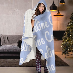 May include: A light blue hooded blanket with the name "Celine" repeated in white text.
