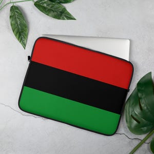 May include: A laptop sleeve featuring a bold design with horizontal stripes of red, black, and green. The sleeve is designed to protect a laptop and has a black zipper. The color scheme is reminiscent of a Pan-African flag.