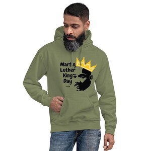 May include: A green hooded sweatshirt with a black and yellow graphic of Martin Luther King Jr. wearing a crown. The text "Martin Luther King Day 2023" is printed below the graphic.