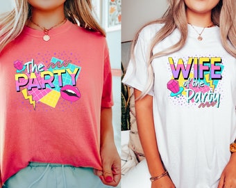 May include: Two t-shirts with a retro 90s design. The pink shirt says "The mr Party" with a pink lip, a diamond, and colorful geometric shapes. The white shirt says "Wife of the Party" with a pink diamond, a lightning bolt, and colorful geometric shapes.