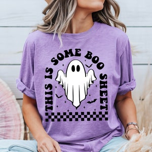 以下が含まれることがあります： 白い幽霊と黒い文字「This is some boo sheet」がプリントされた紫色のTシャツ。幽霊は2つの目があり、コウモリと星に囲まれています。