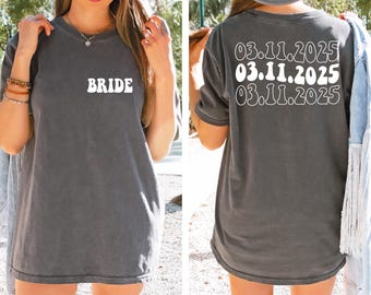Puede incluir: Una camiseta gris de gran tamaño con la palabra "BRIDE" impresa en la parte delantera y la fecha "03.11.2025" impresa tres veces en la parte posterior.