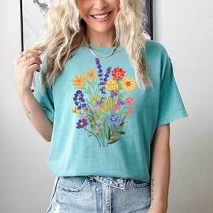 May include: A turquoise blue t-shirt with a colorful floral bouquet print. The flowers are in shades of yellow, orange, red, purple, and blue.
