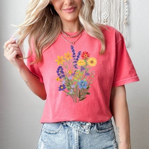 May include: A pink t-shirt with a colorful floral bouquet print. The flowers are in shades of yellow, orange, red, purple, and blue.