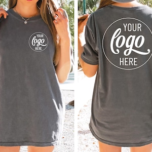 Peut inclure: Un t-shirt gris surdimensionn&eacute; &agrave; manches courtes avec un logo rond blanc qui dit "Votre logo ici" &agrave; l'avant et &agrave; l'arri&egrave;re.
