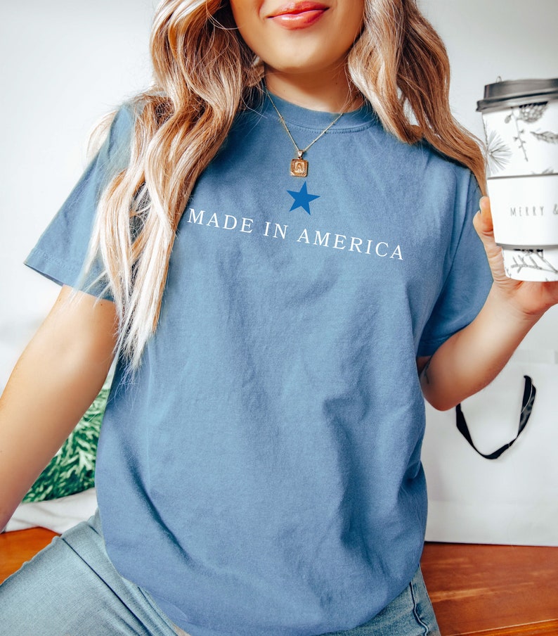 K&ouml;nnte beinhalten: Ein blaues T-Shirt mit einem wei&szlig;en Stern und dem Text "MADE IN AMERICA" auf der Vorderseite.