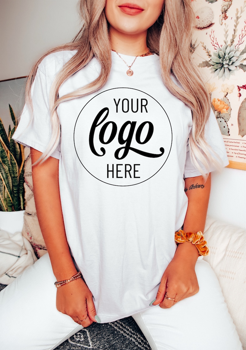 May include: White t-shirt with a black circle on the front that says "YOUR logo HERE" in a cursive font.