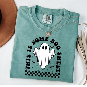 以下が含まれることがあります： 白の幽霊のグラフィックと「This is some boo sheet」というテキストが書かれたターコイズブルーのTシャツです。