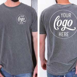 Peut inclure: Un t-shirt gris avec un cercle blanc sur le devant et le dos qui dit "YOUR LOGO HERE" dans une police d'&eacute;criture manuscrite.