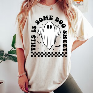 以下が含まれることがあります： 「This is some boo sheet」というテキストと、幽霊の黒いグラフィックが描かれた白いTシャツです。