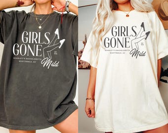 Könnte beinhalten: Zwei übergroße T-Shirts, eines in Anthrazitgrau und eines in Creme, mit dem Text "GIRLS GONE Mild" in einer stilisierten Schriftart. Die Shirts tragen auch den Text "Scarlett's Bachelorette Scottsdale, AZ". Das Design beinhaltet eine Bein-Illustration.