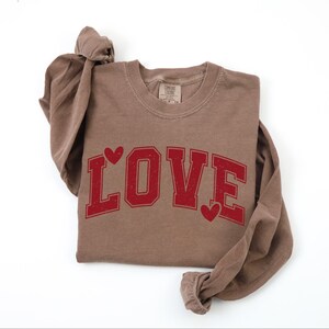 A brown long-sleeved t-shirt with the word "LOVE" printed in red letters.