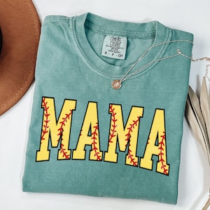 May include: A teal blue t-shirt with the word "MAMA" printed in yellow letters with red stitching, resembling a baseball. The shirt has a distressed look and is made by Comfort Colors.