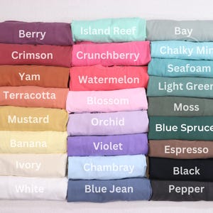 May include: A selection of folded t-shirts in shades like Berry, Crimson, and Yam. Each shirt is labelled with its colour name, including "Island Reef," "Crunchberry," and "Bay." The shirts are neatly stacked, displaying a variety of colours.