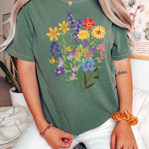 May include: A green t-shirt with a colorful floral print. The flowers are in shades of yellow, red, blue, purple, and pink.