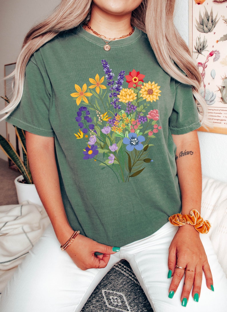 May include: A green t-shirt with a colorful floral print. The flowers are in shades of yellow, red, blue, purple, and pink.