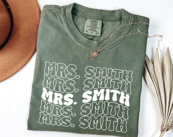 May include: A green t-shirt with the text "MRS. SMITH" repeated five times in a white retro font.
