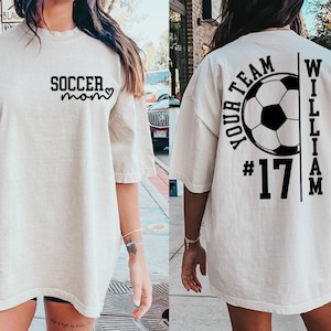 May include: Cream-colored oversized t-shirt with black text. The front reads "SOCCER mom" with a heart. The back features a soccer ball graphic, the words "YOUR TEAM" and "WILLIAM", and the number "17".