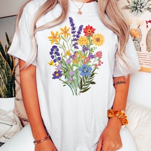 May include: White t-shirt with a colorful floral bouquet print. The flowers are in shades of yellow, red, purple, blue, and green.