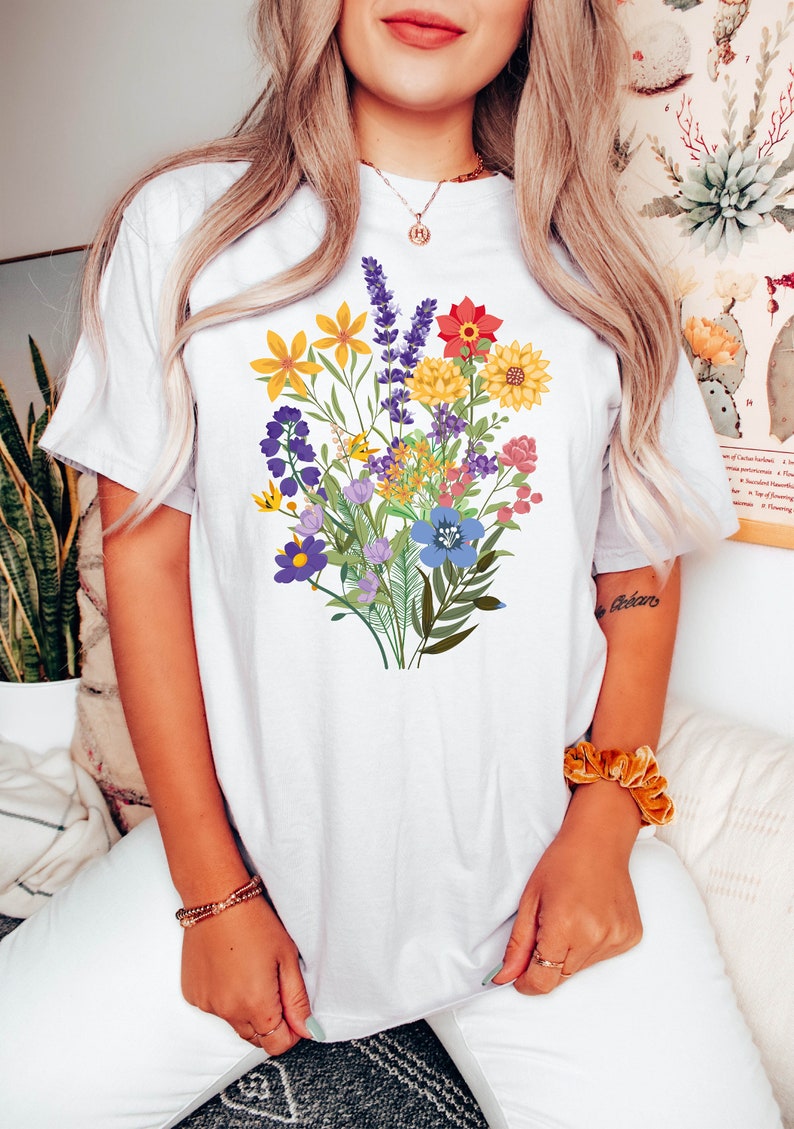 May include: White t-shirt with a colorful floral bouquet print. The flowers are in shades of yellow, red, purple, blue, and green.