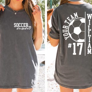 May include: Dark gray t-shirt with the text "soccer mom" in white on the front. The back of the shirt features a soccer ball graphic, the words "YOUR TEAM", the number "17", and the name "WILLIAM".