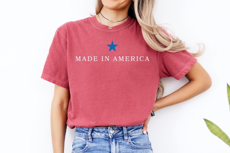 K&ouml;nnte beinhalten: Ein rotes T-Shirt mit einem blauen Stern und dem Text "MADE IN AMERICA" auf der Vorderseite.