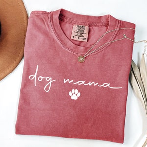 May include: A red t-shirt with the text "dog mama" in white script with a white paw print below.