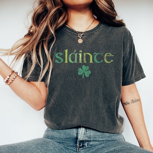 May include: A dark gray t-shirt with a green and yellow graphic that says "sl&aacute;inte" and a green shamrock.