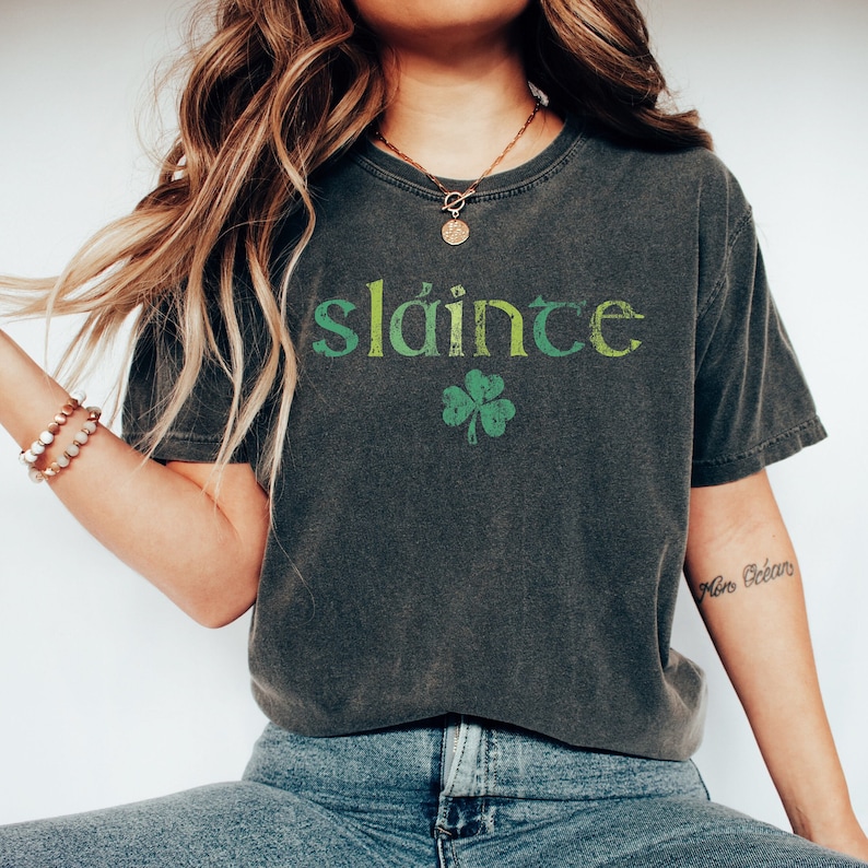 May include: A dark gray t-shirt with a green and yellow graphic that says "sl&aacute;inte" and a green shamrock.
