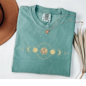 K&ouml;nnte beinhalten: Ein blaues T-Shirt mit einem Grafikdruck eines himmlischen Designs mit Erde, Sonne und Mond. Das Shirt hat ein Etikett mit der Aufschrift "Comfort Colors" und "S - P - CH".