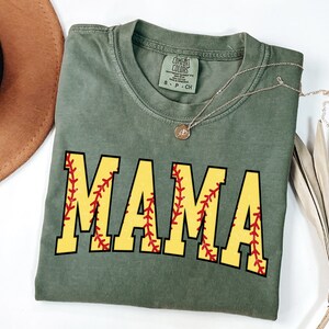 May include: A green t-shirt with the word "MAMA" in yellow letters with a red baseball stitch design.