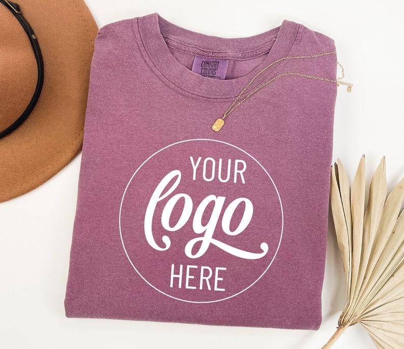 May include: A mauve coloured t-shirt with a white circle that says "YOUR logo HERE" in a cursive font.