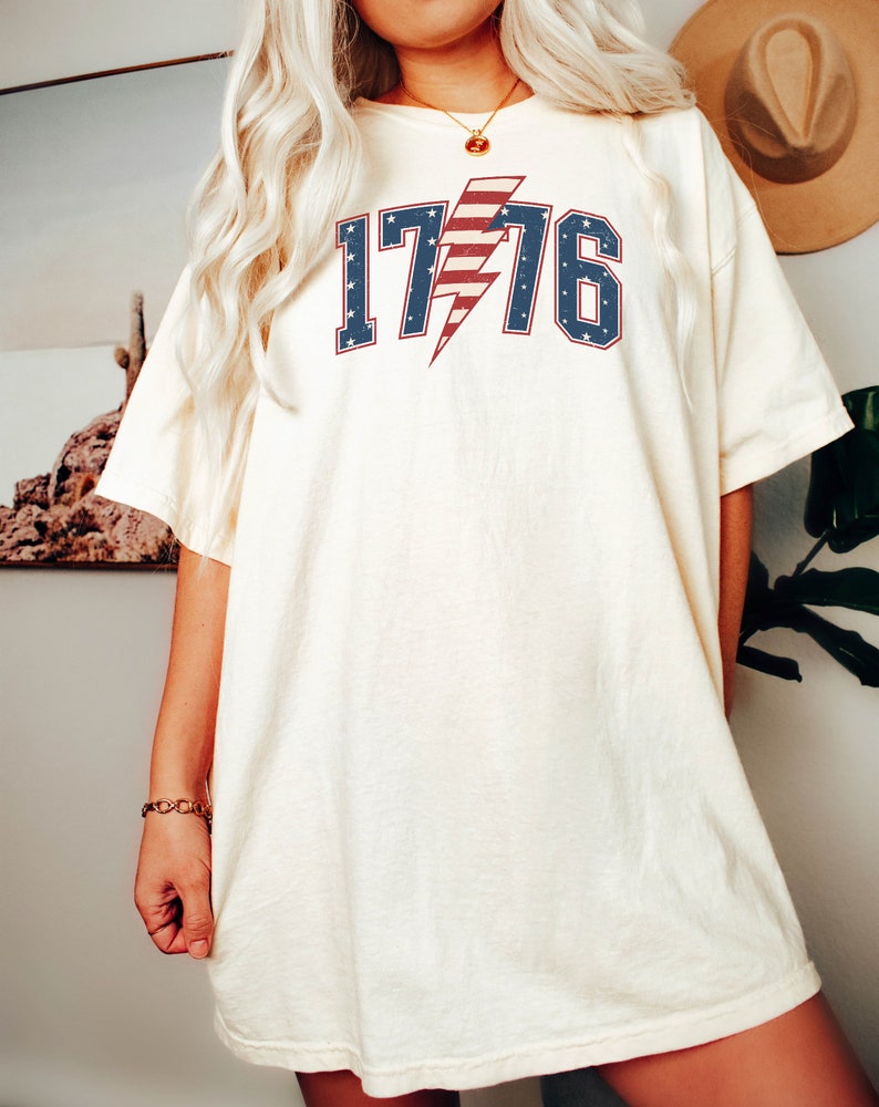 May include: A white oversized t-shirt with a red, white, and blue lightning bolt graphic and the text "1776".