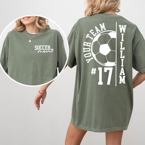 May include: Olive green t-shirt with white text and a soccer theme. The front says "Soccer Mom" with a heart. The back features a soccer ball graphic, the words "Your Team", the number "17", and the name "William".