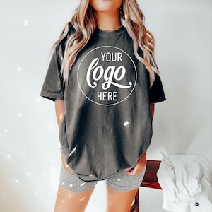 May include: An oversized dark grey t-shirt with a white circle on the front that says "YOUR logo HERE" in a handwritten font.