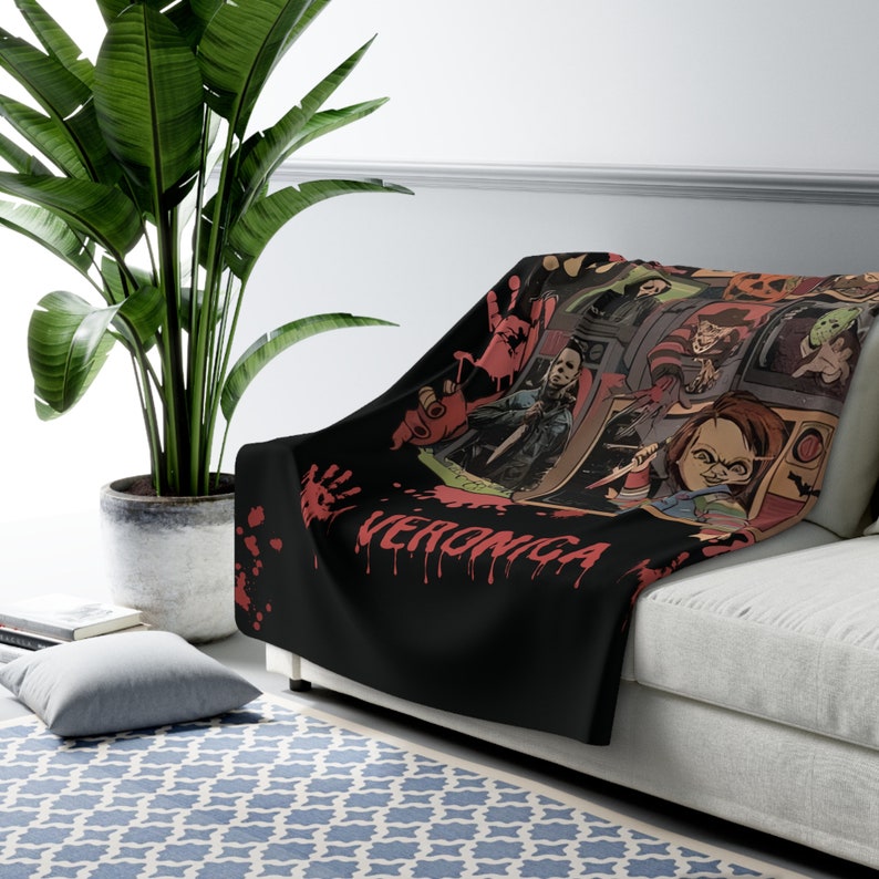 May include: Black throw blanket with a horror movie theme. The blanket features images of iconic horror movie characters like Freddy Krueger, Jason Voorhees, and Chucky. The text "Veronica" is written in red on the blanket.